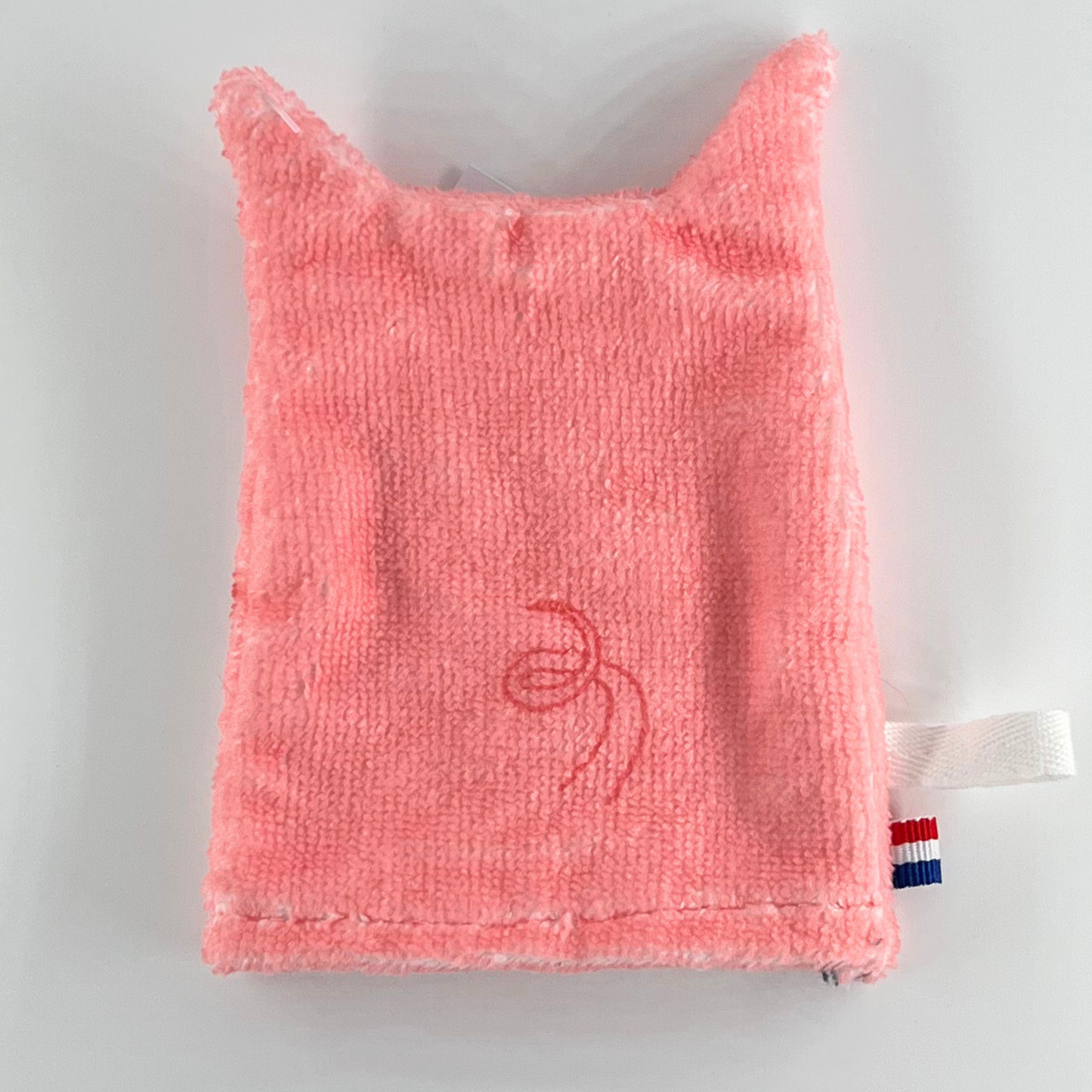 Baksidan av en rosa tvättlapp i form av en gris, med en enkel svans och enfärgad yta.