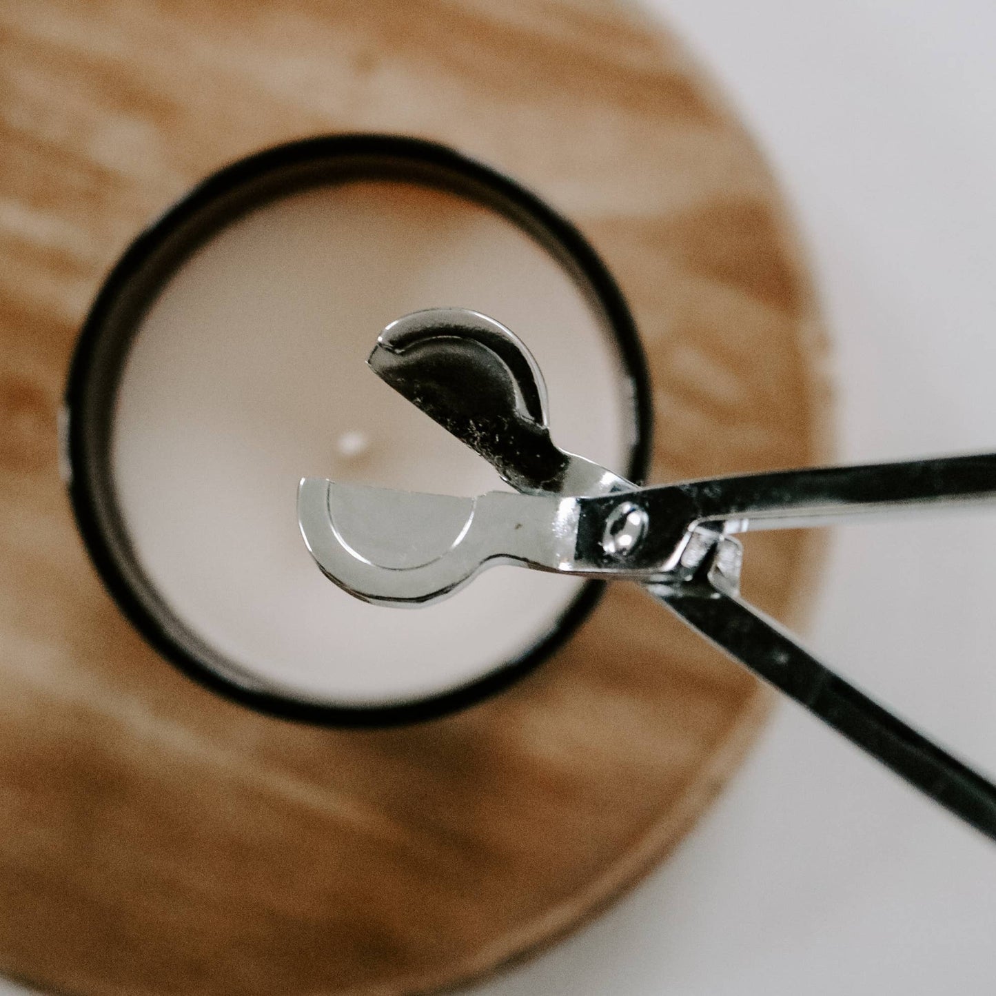 Närbild ovanifrån på vektrimmer i silverfärg, som används för att klippa av veken på ett ljus i ett svart glas. Ljussax, veksax, vekesax, veketrimmer, vek-trimmer.