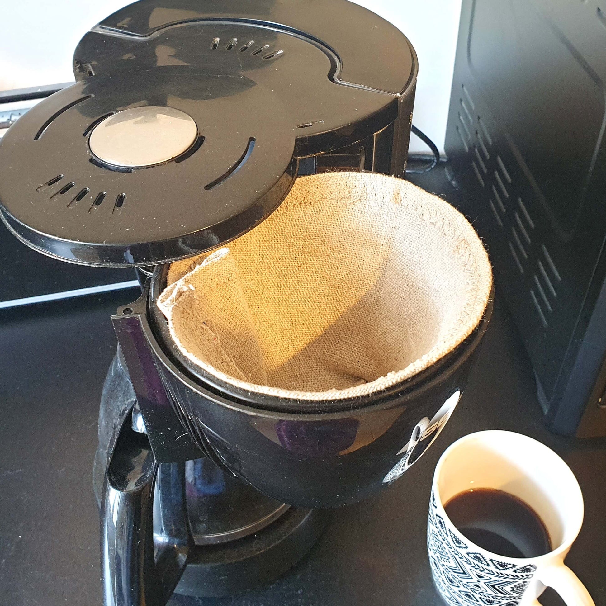 Återanvändbart kaffefilter i linne, storlek 4, placerat i en kaffebryggare bredvid en kopp nybryggt kaffe. Ett hållbart alternativ för en mer miljövänlig kaffevana.