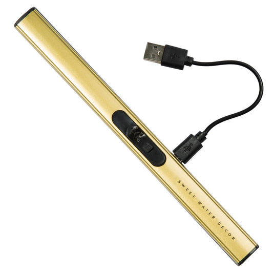 Elektrisk tändare i guldfärg, liggandes diagonalt på vit bakgrund. Kort, svart laddsladd inkopplad med USB. Laddningssladd.
