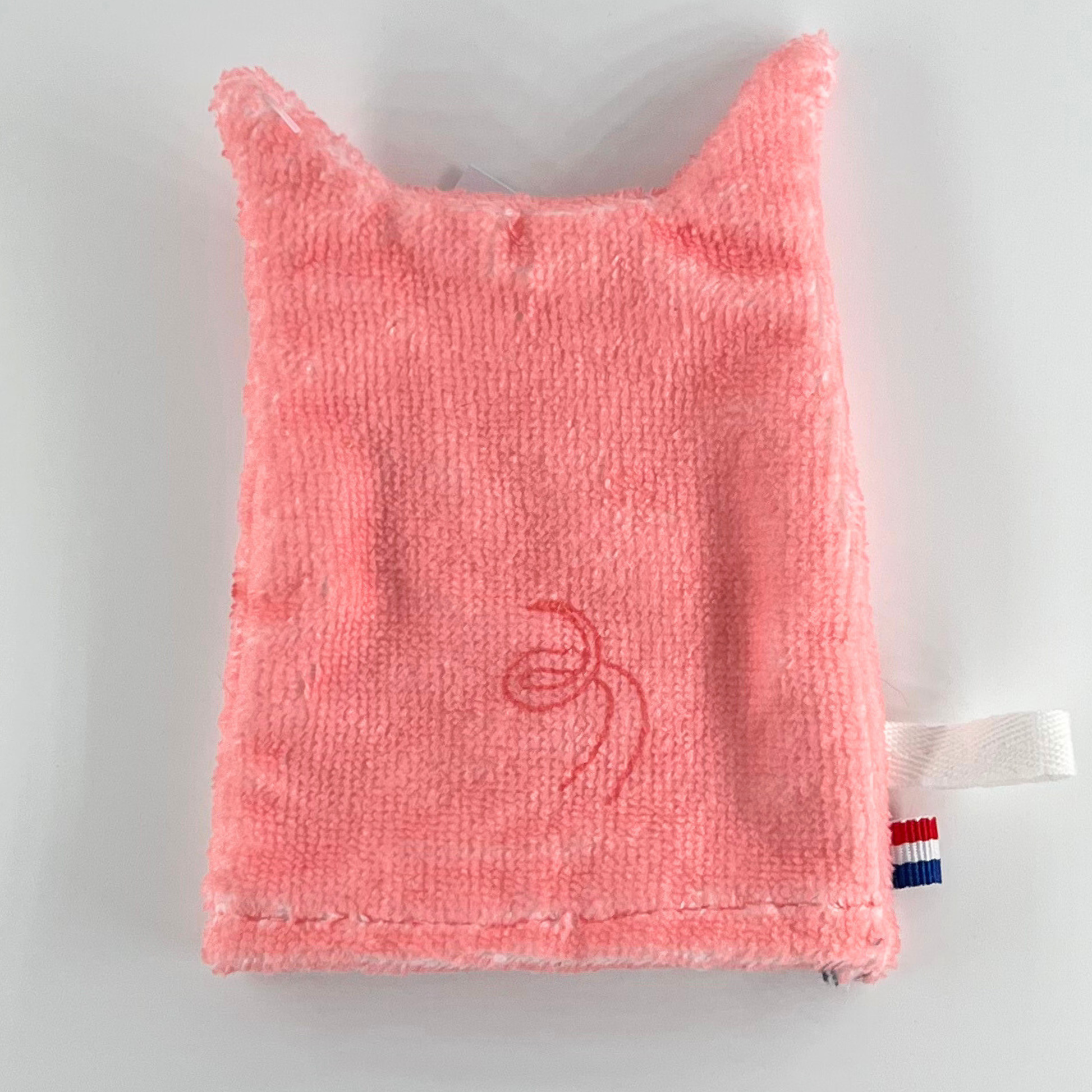 Baksidan av en rosa tvättlapp i form av en gris, med en enkel svans och enfärgad yta.