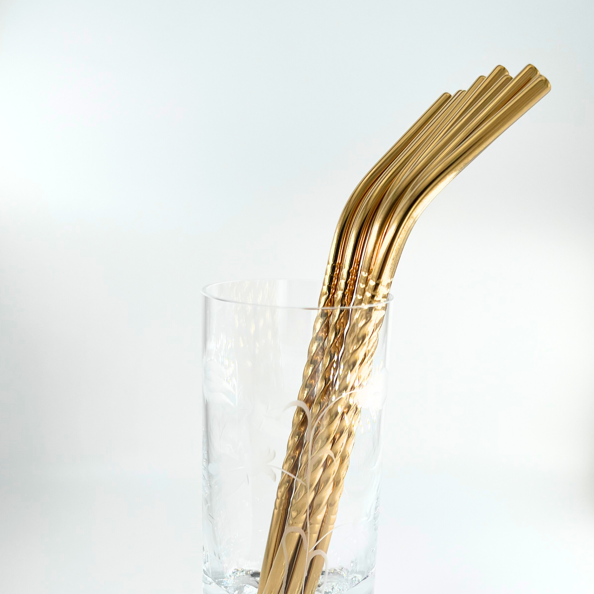 Bukett av sugrör i metall i ett glas. Böjda med spiraldesign i guldfärg, vända åt höger.