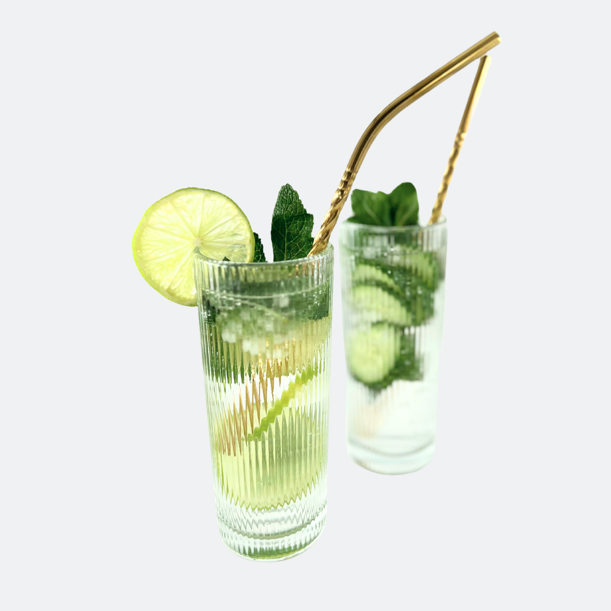 Två drinkar i ribbade glas, med lime, is och mynta i. Böjt sugrör i rostfritt stål, med spiraldesign i guldfärg, vänt åt höger.