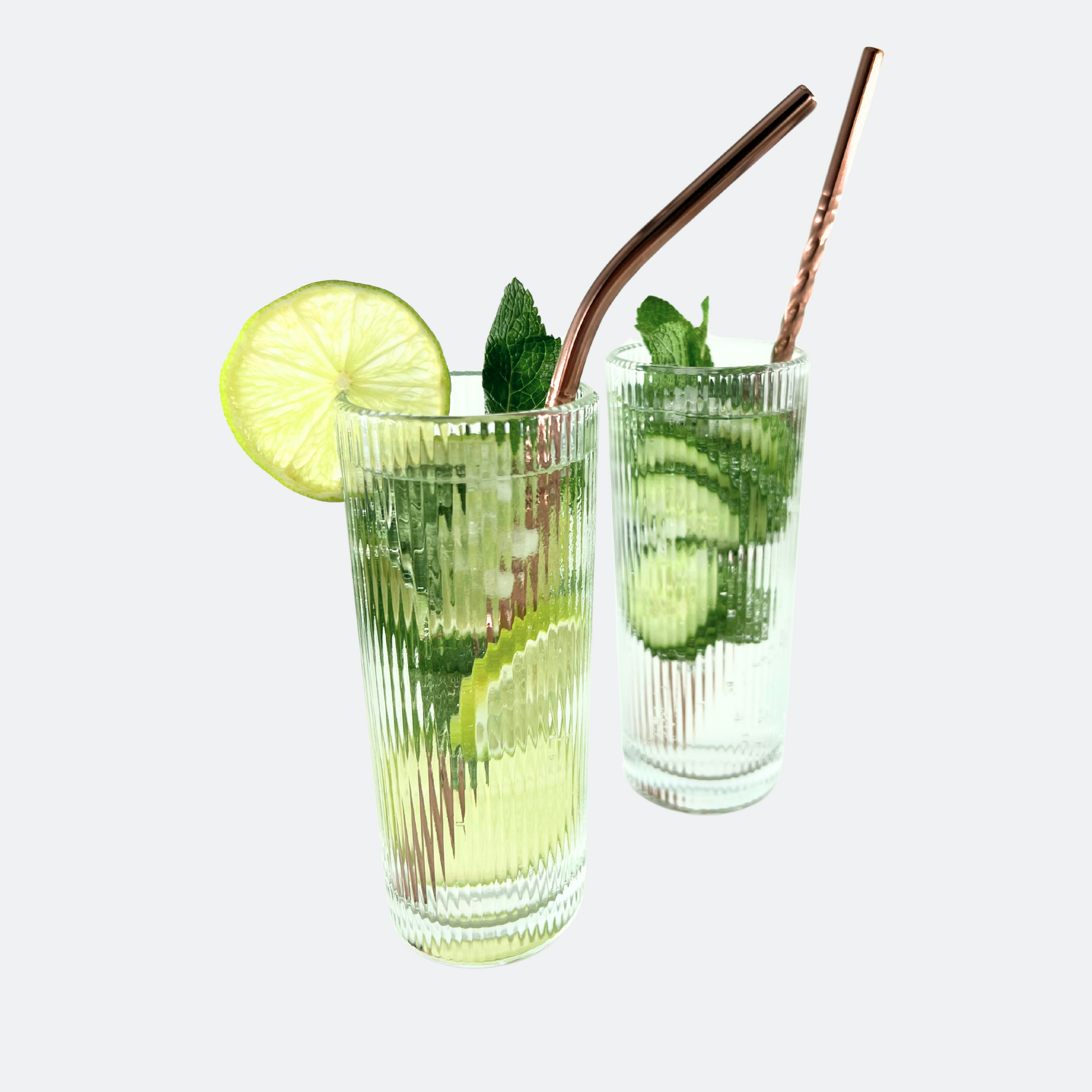 Två drinkar i ribbade glas, med lime, gurka, is och mynta i. Böjt sugrör i rostfritt stål, med spiraldesign i roséguld, vänt åt höger.