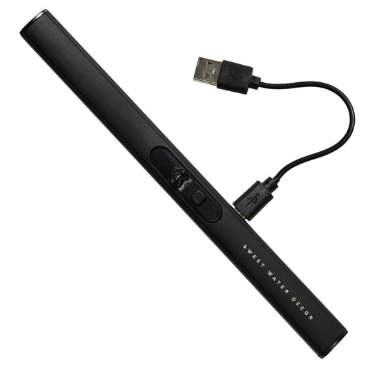 Elektrisk tändare i mattsvart, liggandes på vit bakgrund. Kort, svart laddsladd inkopplad med USB. Svart färg. Laddningssladd.